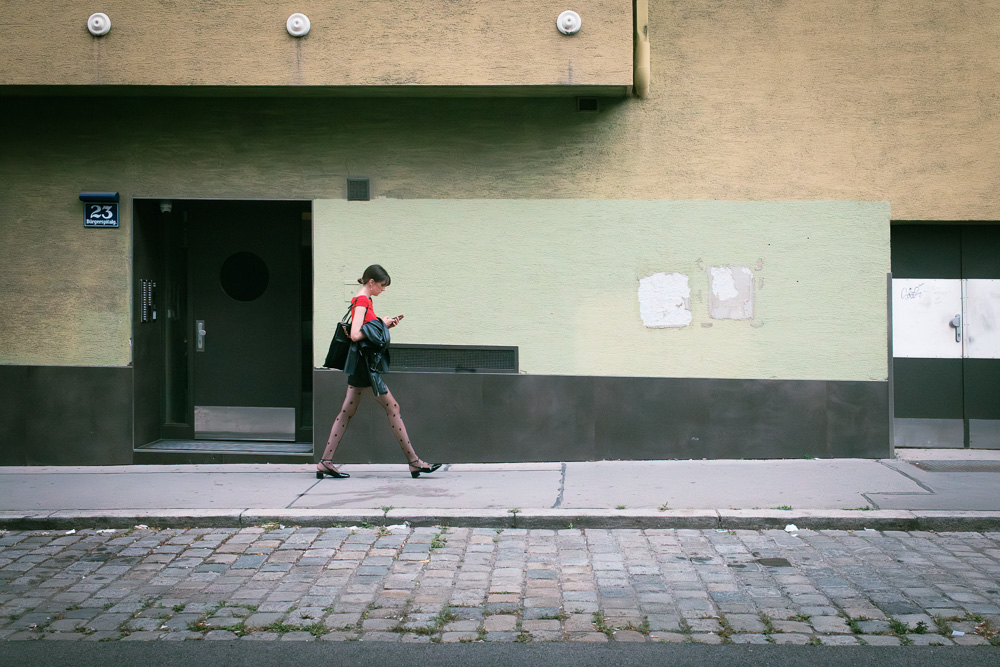 Eine Frau im roten Kleid geht auf dem Gehweg einer Straße und blickt auf ihr Handy.
